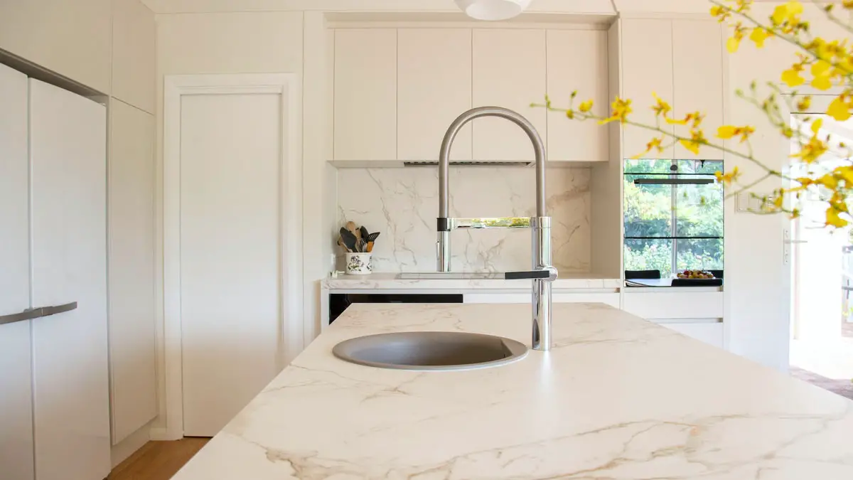 White kitchen featuring a marble countertop with stainless steel sink