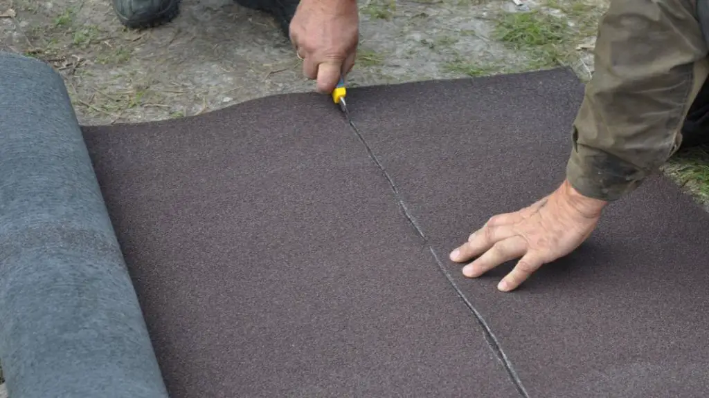 Construction worker cutting roll roofing felt