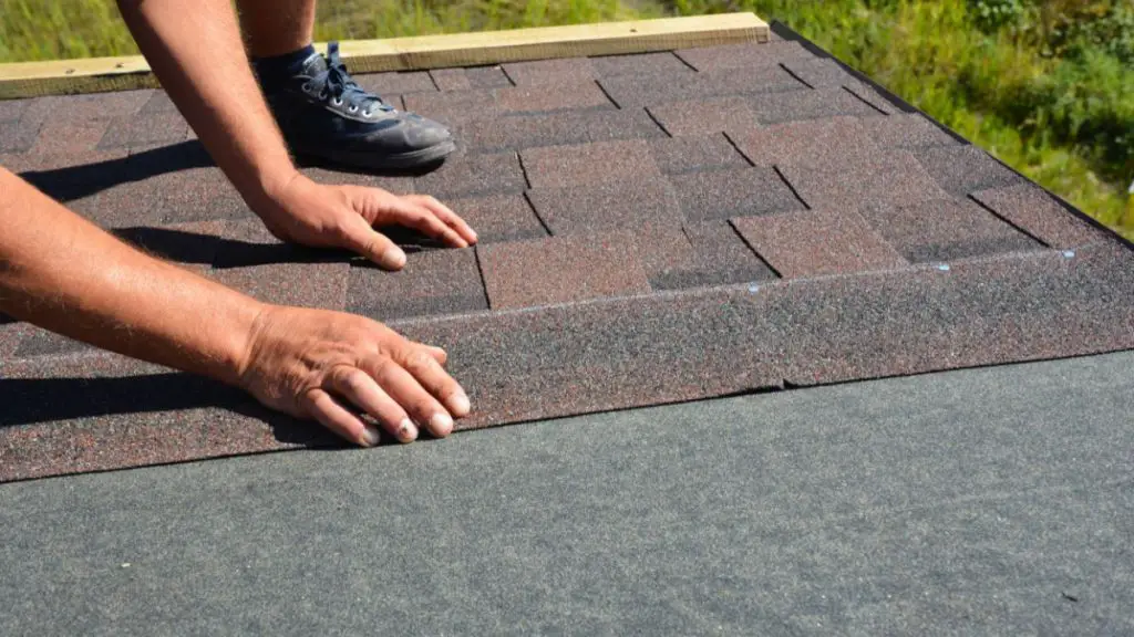Roofer hands laying asphalt shingles on house construction roof.