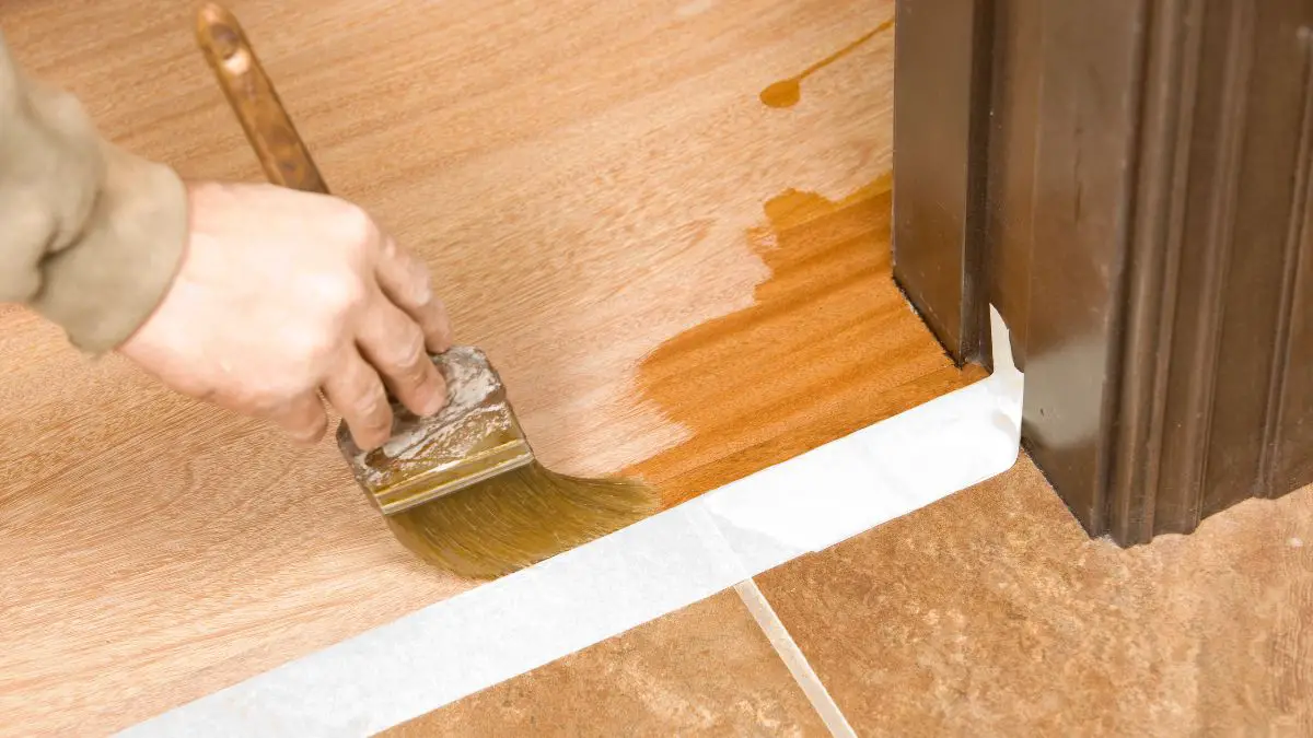 Painter Brushing Clear Polyurethane on Hardwood Floor.
